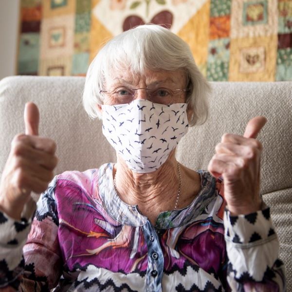 Senior woman wearing a COVID-19 mask and giving a thumbs-up gesture