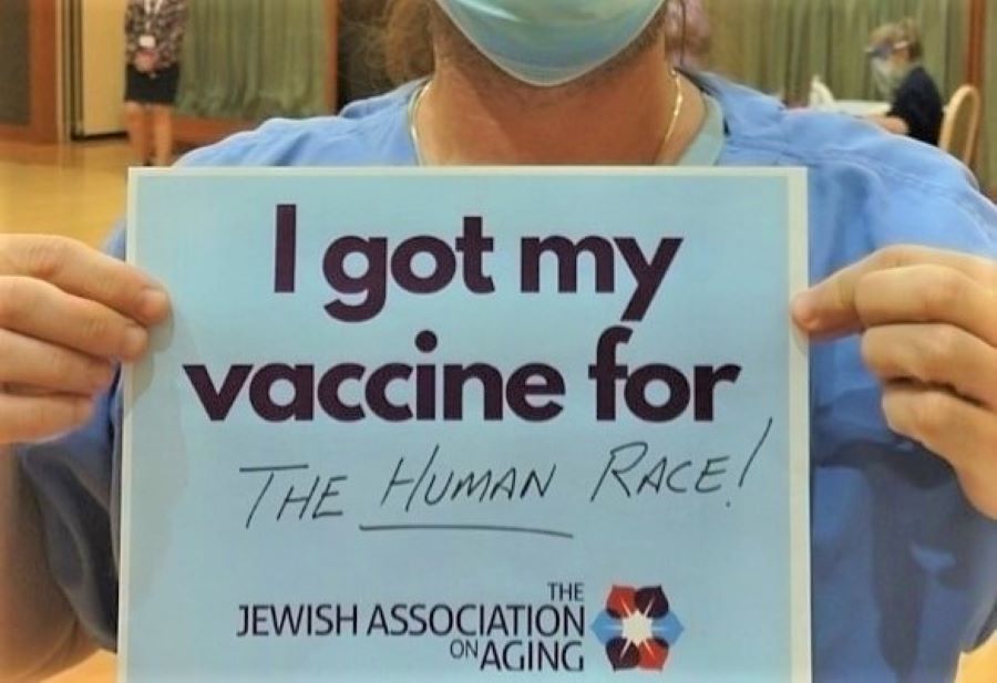 Jewish Association on Aging nurse holding a sign stating "I got my vaccine for the human race!"
